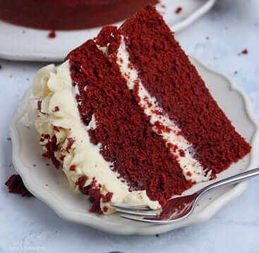 Slice of rich red velvet cake with cream cheese frosting on plate, showcasing the luxurious texture from Premix Red Velvet Cake & Cupcake Mix - Restaurant Quality Baking.